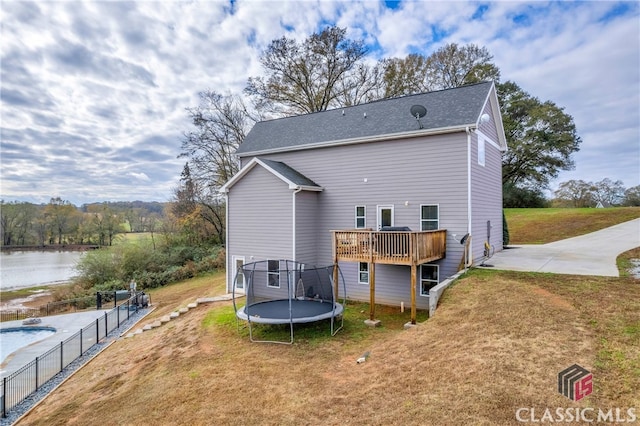 rear view of house with a deck with water view, a yard, and a trampoline