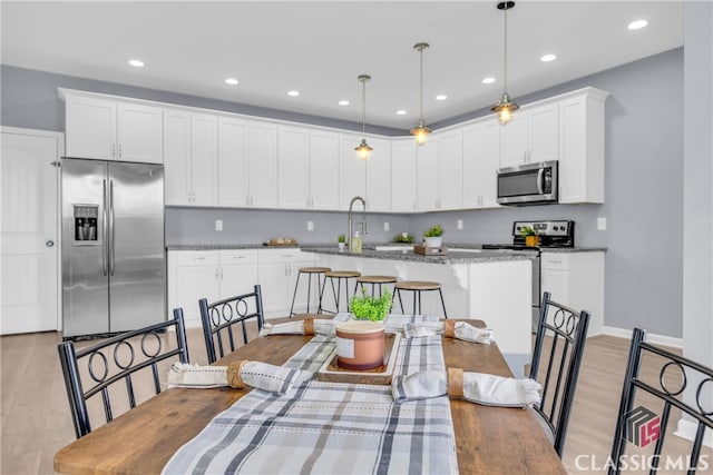 kitchen featuring white cabinetry, hanging light fixtures, light stone counters, appliances with stainless steel finishes, and light wood-type flooring