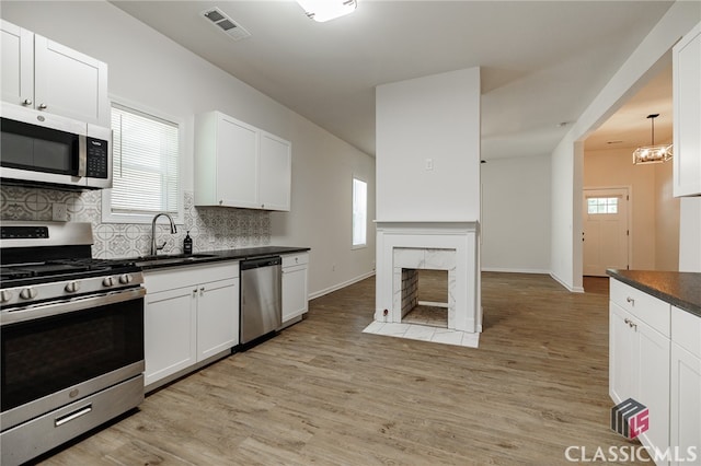 kitchen featuring stainless steel appliances, a premium fireplace, a sink, visible vents, and dark countertops