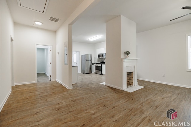 interior space with attic access, visible vents, baseboards, a tiled fireplace, and light wood-style floors