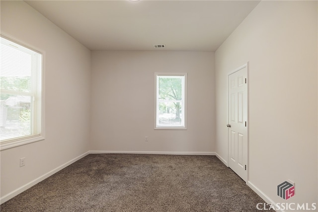 spare room with dark colored carpet, visible vents, and baseboards