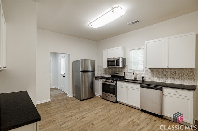 kitchen with appliances with stainless steel finishes, light wood-type flooring, sink, and white cabinets