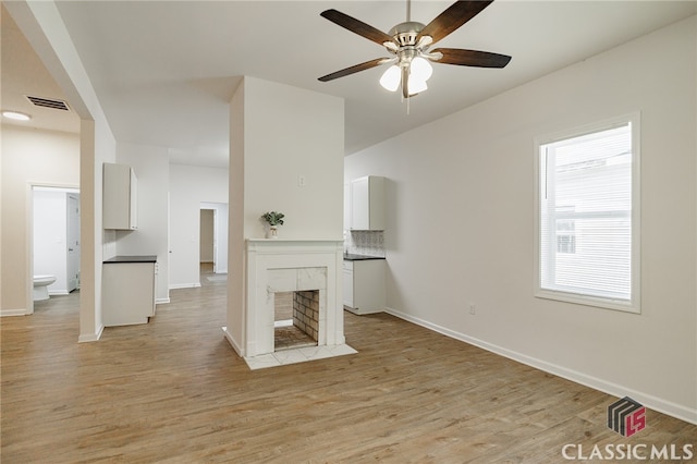 unfurnished living room with light wood-style floors, a tile fireplace, visible vents, and baseboards