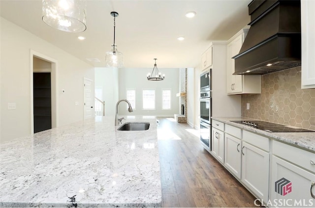 kitchen with premium range hood, white cabinetry, sink, light stone countertops, and black electric cooktop