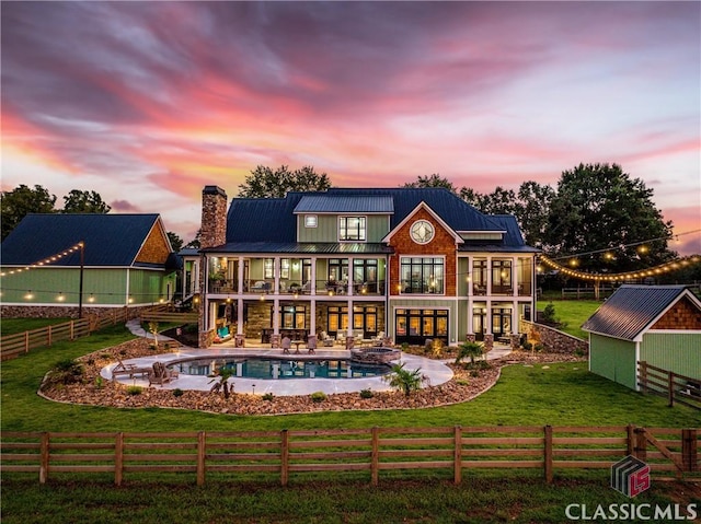 back house at dusk featuring a lawn, a patio, a balcony, a storage unit, and a fenced in pool