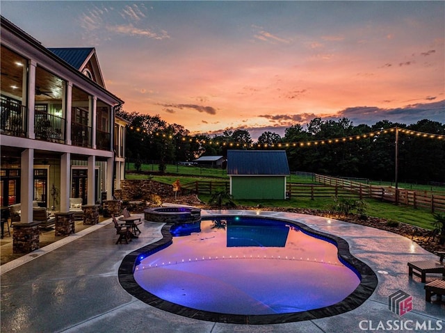 pool at dusk with an in ground hot tub, a patio, and a shed