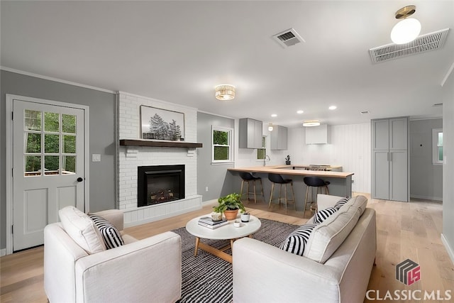 living room featuring ornamental molding, light wood-type flooring, a brick fireplace, and sink