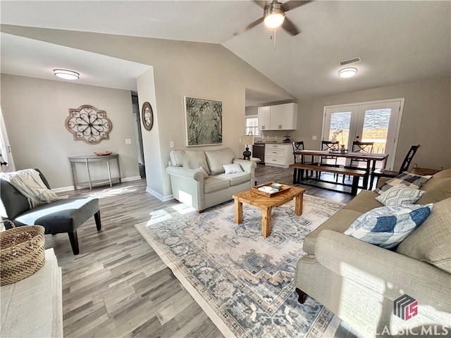 living room featuring ceiling fan, french doors, lofted ceiling, and light wood-type flooring