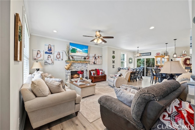 living room with ceiling fan, ornamental molding, a stone fireplace, and light hardwood / wood-style floors