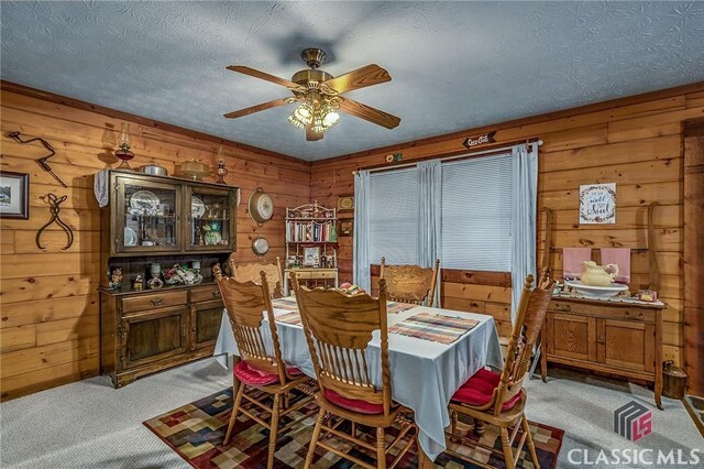 dining area with wood walls, ceiling fan, light carpet, and a textured ceiling