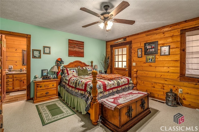 carpeted bedroom featuring a textured ceiling, ceiling fan, wood walls, and ensuite bathroom