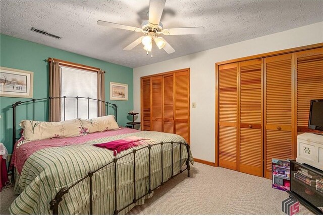 carpeted bedroom featuring a textured ceiling, ceiling fan, and multiple closets