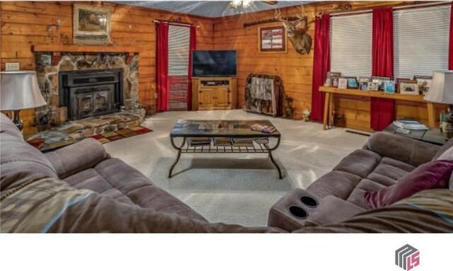 carpeted living room with ceiling fan, wood walls, and a stone fireplace