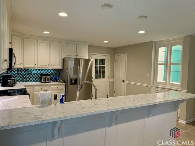 kitchen featuring decorative backsplash, white cabinets, light stone countertops, and stainless steel appliances