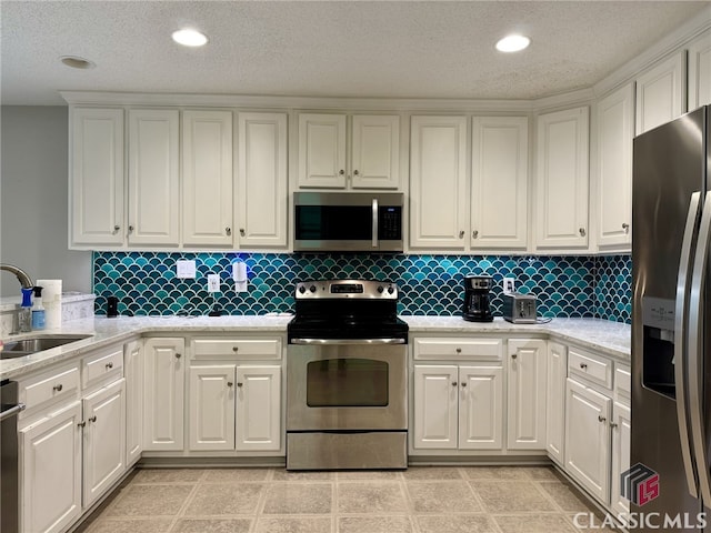 kitchen featuring sink, light stone countertops, white cabinetry, appliances with stainless steel finishes, and tasteful backsplash