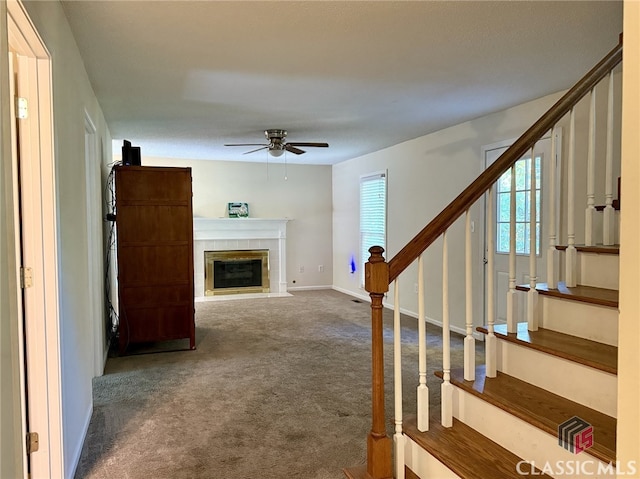 unfurnished living room featuring a tiled fireplace, carpet floors, and ceiling fan