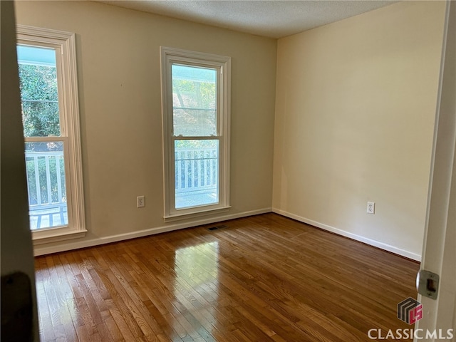 unfurnished room with a wealth of natural light, a textured ceiling, and hardwood / wood-style flooring