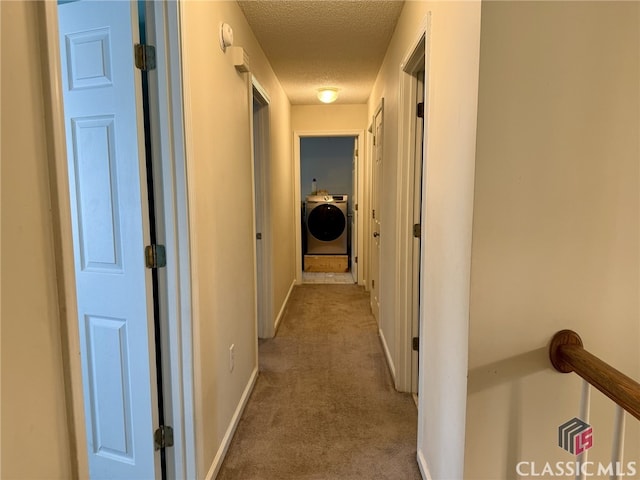 hall with washer / dryer, a textured ceiling, and light carpet