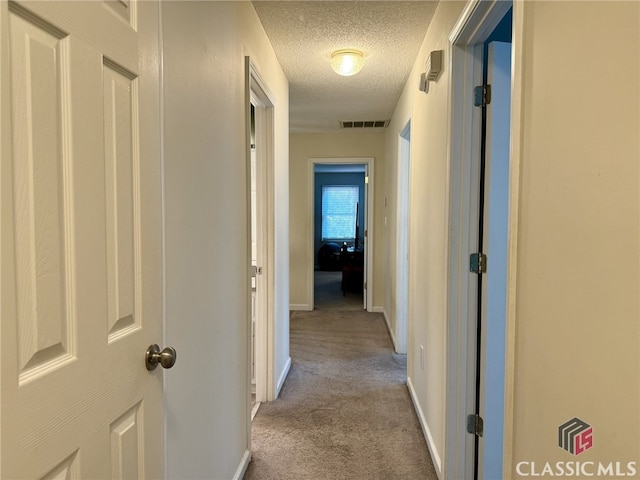 hallway featuring a textured ceiling and light colored carpet