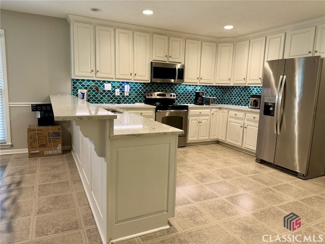 kitchen featuring kitchen peninsula, a breakfast bar area, appliances with stainless steel finishes, backsplash, and white cabinetry