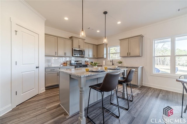 kitchen featuring a kitchen island, a kitchen bar, dark wood-type flooring, appliances with stainless steel finishes, and light stone counters