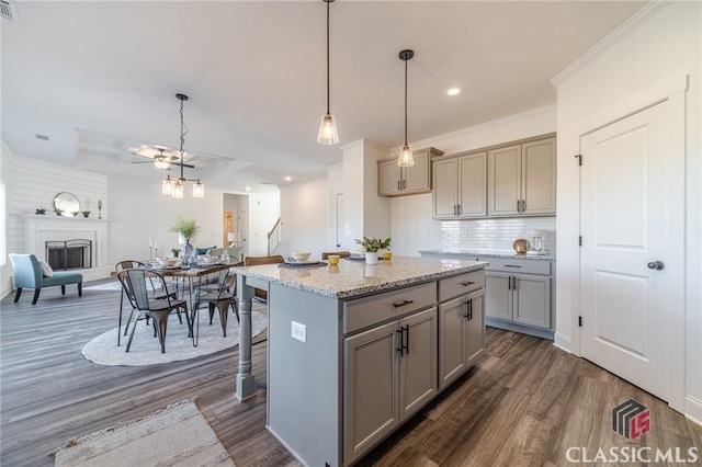 kitchen with light stone countertops, a center island, hanging light fixtures, gray cabinetry, and a breakfast bar area