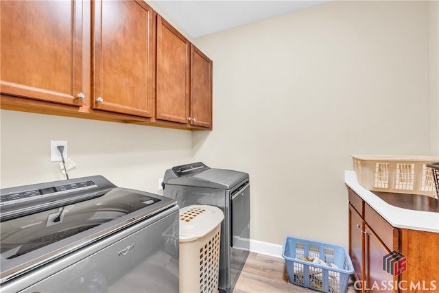 washroom with light wood-type flooring, washing machine and clothes dryer, and cabinets