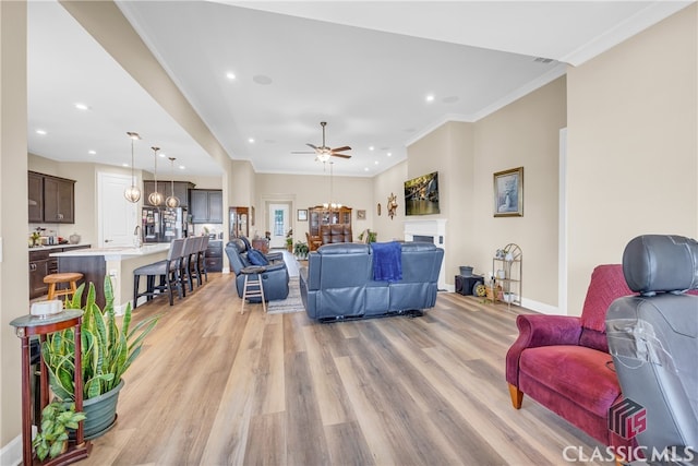 living room with ceiling fan with notable chandelier, crown molding, sink, and light hardwood / wood-style floors