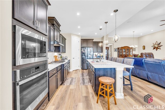 kitchen with a kitchen bar, stainless steel appliances, light wood-type flooring, and a center island with sink