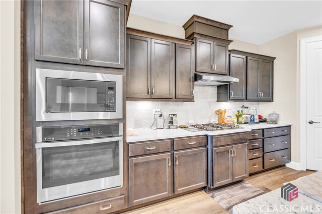 kitchen featuring appliances with stainless steel finishes, dark brown cabinetry, decorative backsplash, and light hardwood / wood-style floors