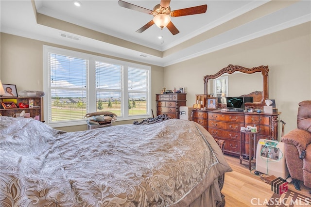 bedroom featuring light hardwood / wood-style flooring, ceiling fan, ornamental molding, and a tray ceiling