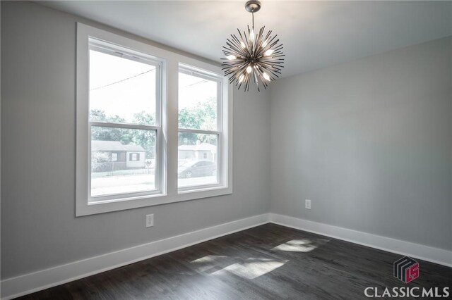 empty room with a notable chandelier and dark wood-type flooring