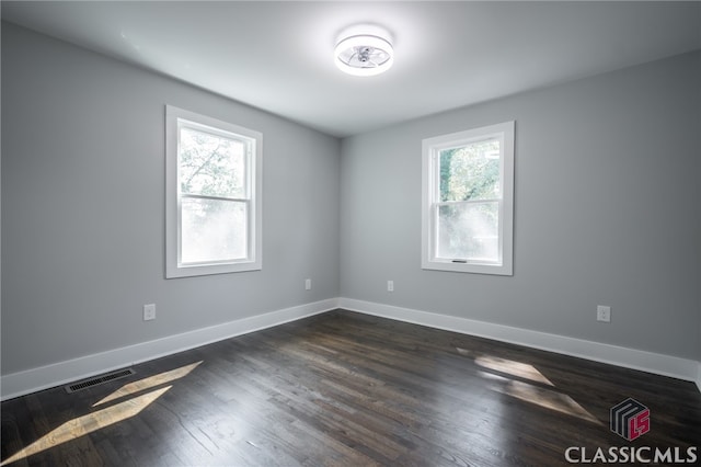 empty room with a wealth of natural light and dark hardwood / wood-style flooring