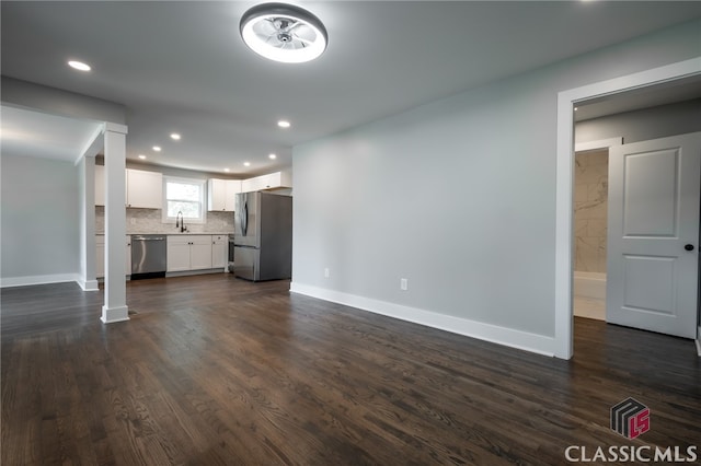 unfurnished living room featuring decorative columns, sink, and dark wood-type flooring