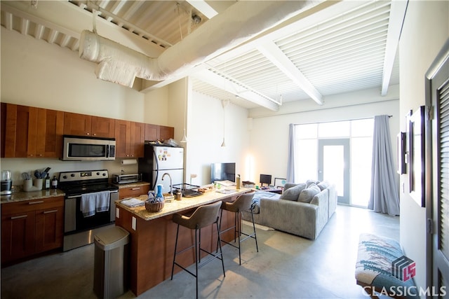 kitchen featuring beam ceiling, concrete floors, a center island with sink, stainless steel appliances, and a kitchen bar