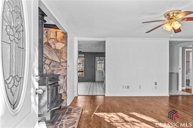 unfurnished living room with ceiling fan, dark hardwood / wood-style flooring, a wood stove, and ornamental molding