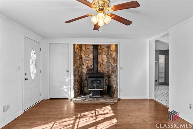 unfurnished living room with a wood stove, ceiling fan, crown molding, and hardwood / wood-style flooring