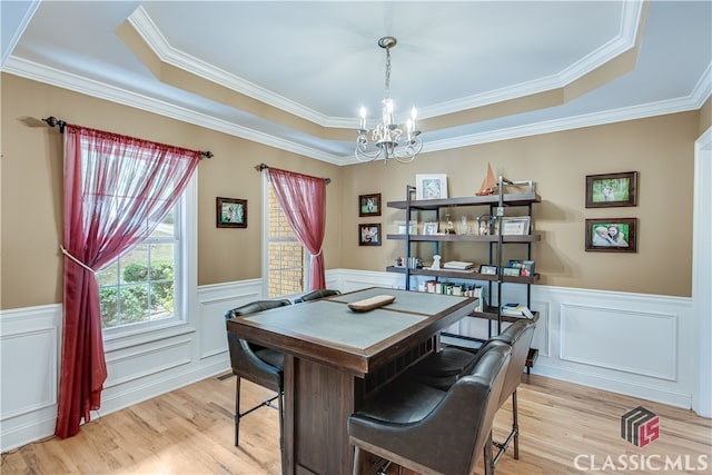 office space featuring ornamental molding, light wood-type flooring, a tray ceiling, and an inviting chandelier