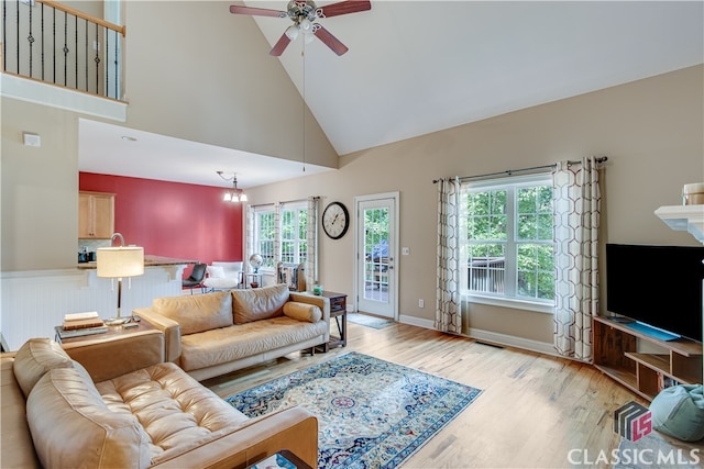 living room with light wood-type flooring, ceiling fan with notable chandelier, and high vaulted ceiling