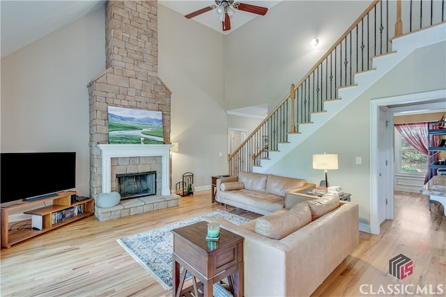 living room featuring ceiling fan, a stone fireplace, light wood-type flooring, and high vaulted ceiling