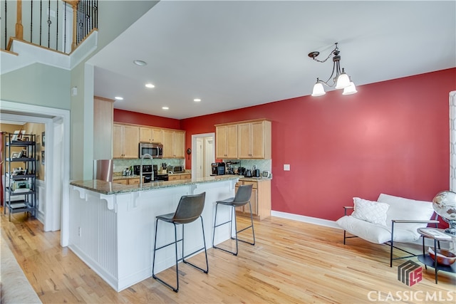 kitchen with tasteful backsplash, kitchen peninsula, light hardwood / wood-style flooring, light brown cabinets, and stone countertops