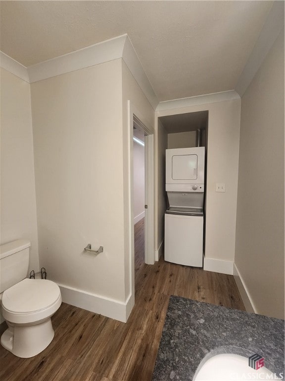 bathroom featuring vanity, wood-type flooring, stacked washing maching and dryer, crown molding, and toilet