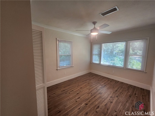 spare room featuring ornamental molding, a wealth of natural light, ceiling fan, and dark wood-type flooring