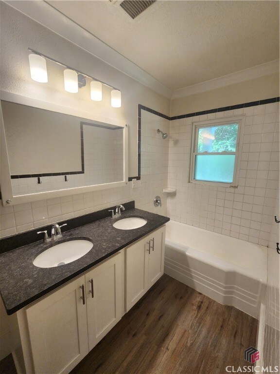 bathroom with tasteful backsplash, vanity, tiled shower / bath combo, hardwood / wood-style flooring, and ornamental molding