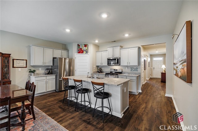 kitchen featuring an island with sink, stainless steel appliances, white cabinetry, and dark wood-type flooring