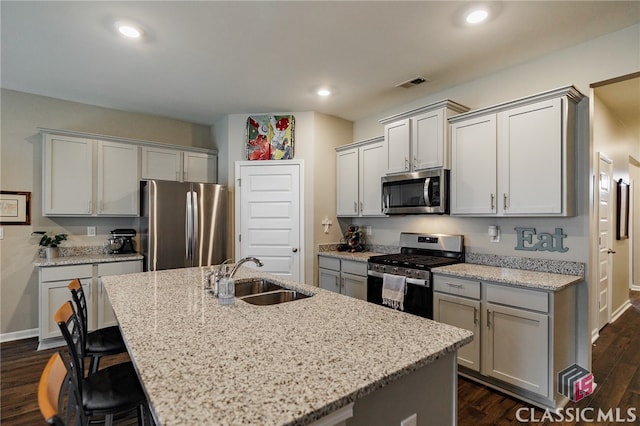 kitchen with appliances with stainless steel finishes, dark wood-type flooring, an island with sink, light stone counters, and sink