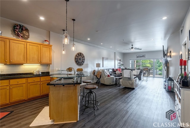 kitchen with hanging light fixtures, tasteful backsplash, a breakfast bar area, dark hardwood / wood-style flooring, and a center island with sink