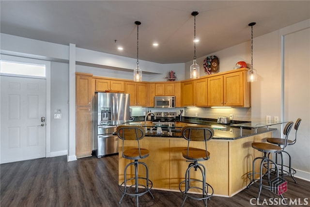 kitchen featuring kitchen peninsula, backsplash, appliances with stainless steel finishes, a kitchen bar, and dark hardwood / wood-style flooring