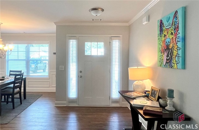 foyer entrance with a notable chandelier, dark wood-type flooring, a wealth of natural light, and ornamental molding