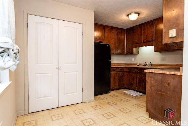 kitchen featuring a textured ceiling, sink, black refrigerator, and wood counters